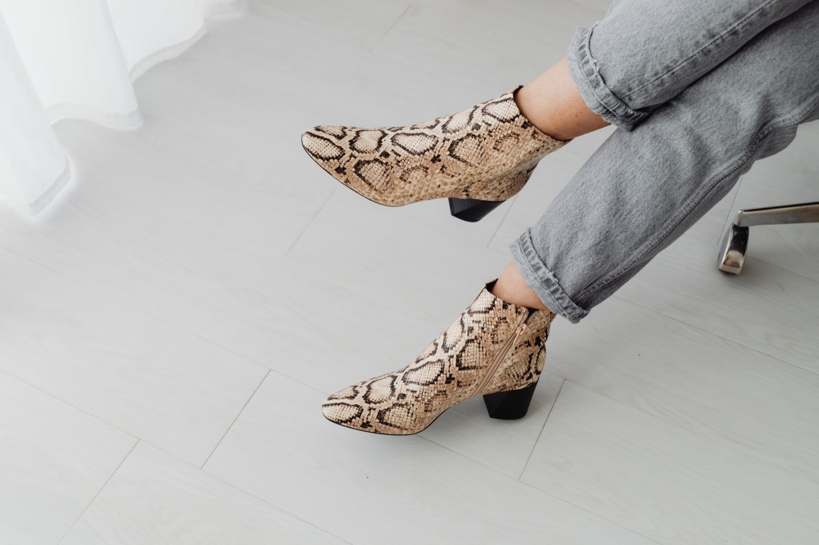 Snake-print ankle boots worn with cuffed grey jeans on a pale floor.